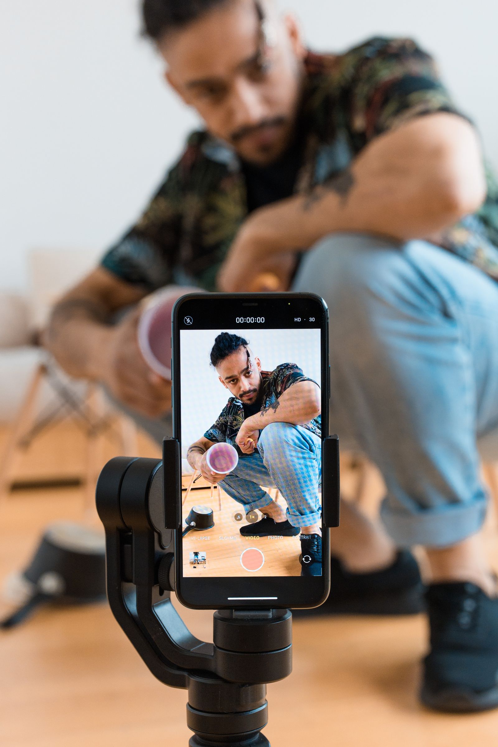A man recording a video of himself on a smartphone mounted on a tripod indoors