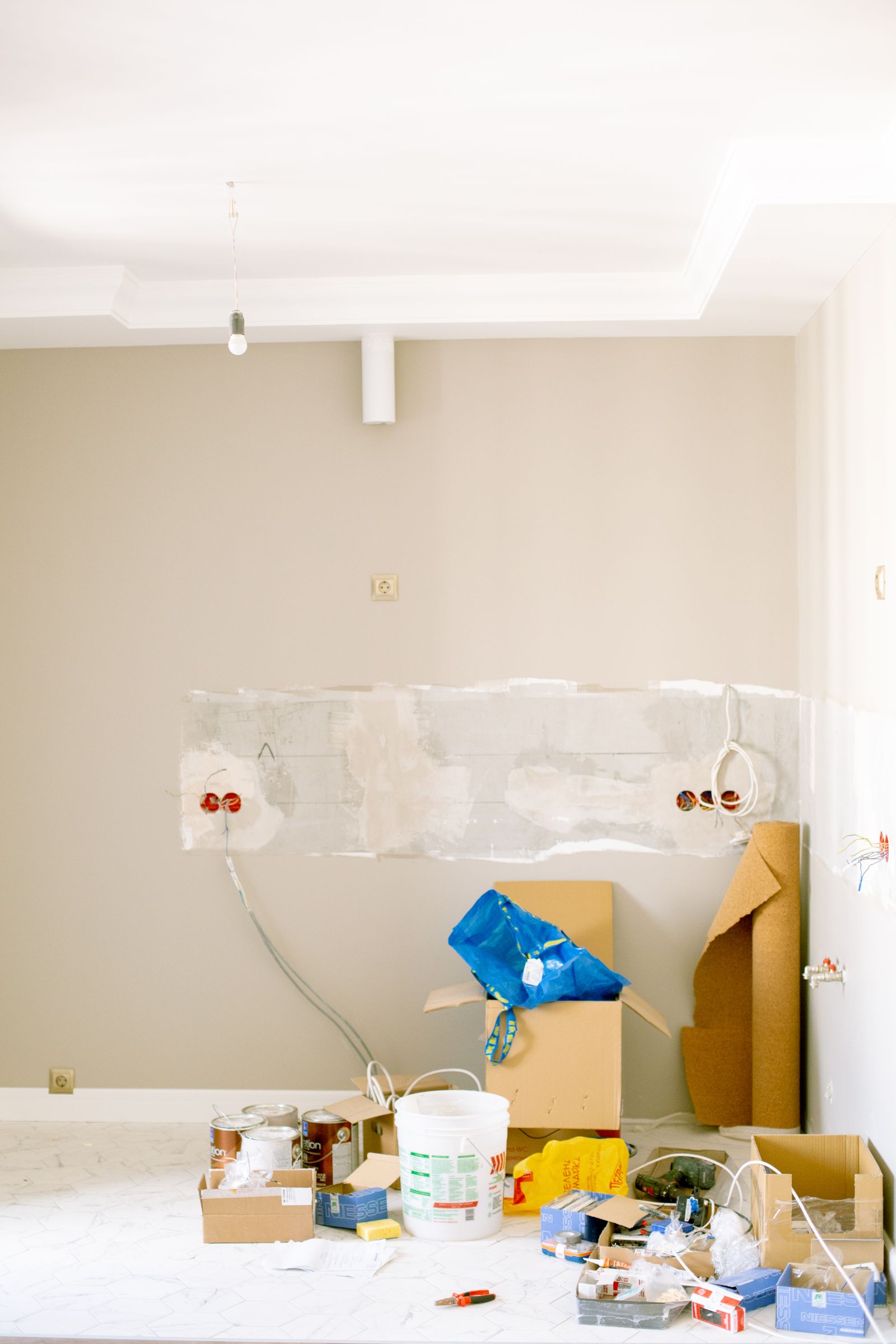 A room mid-renovation with paint cans, tools, drop cloths, and materials spread across the floor.