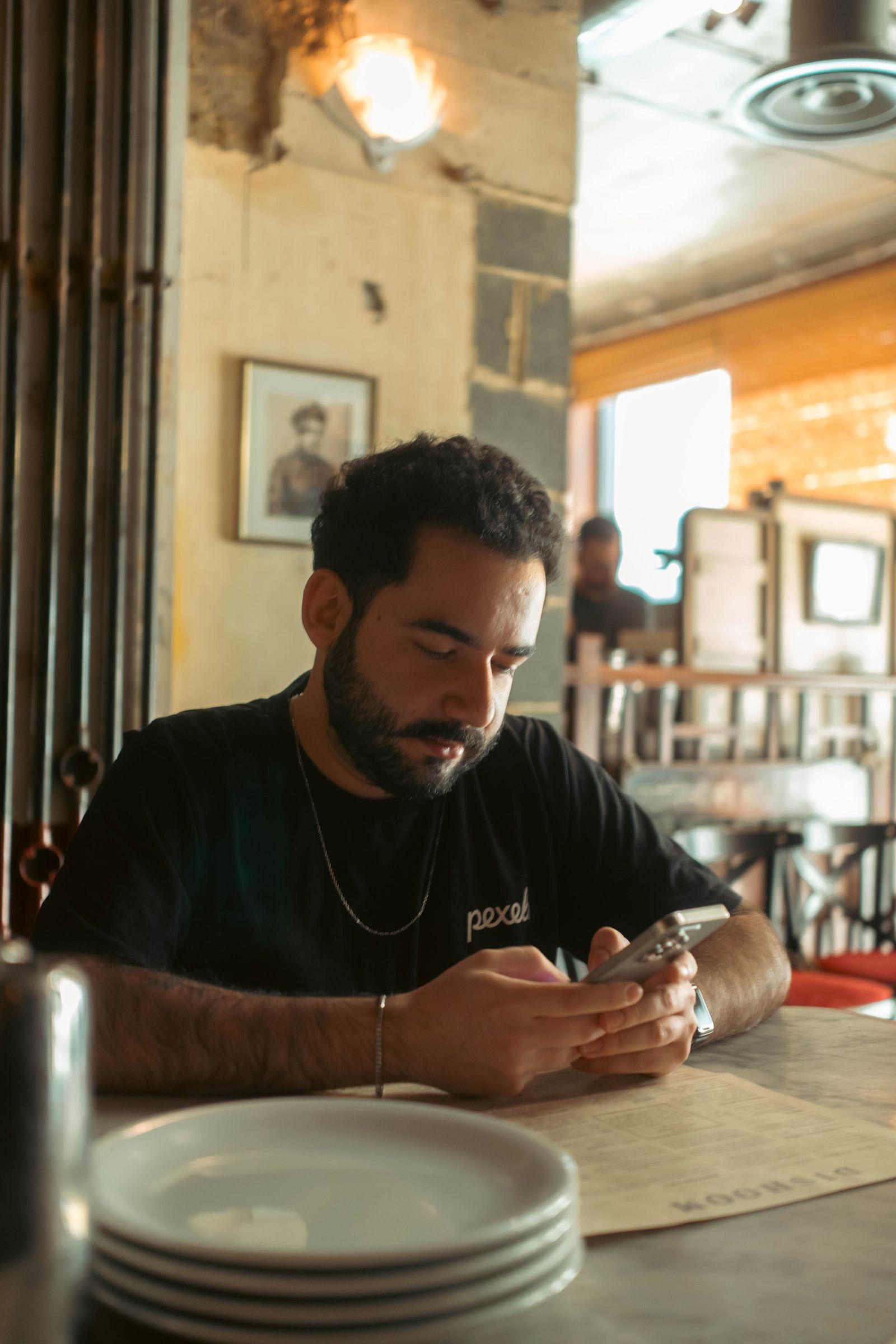 A young man sitting at a cafe table watching something on his smartphone