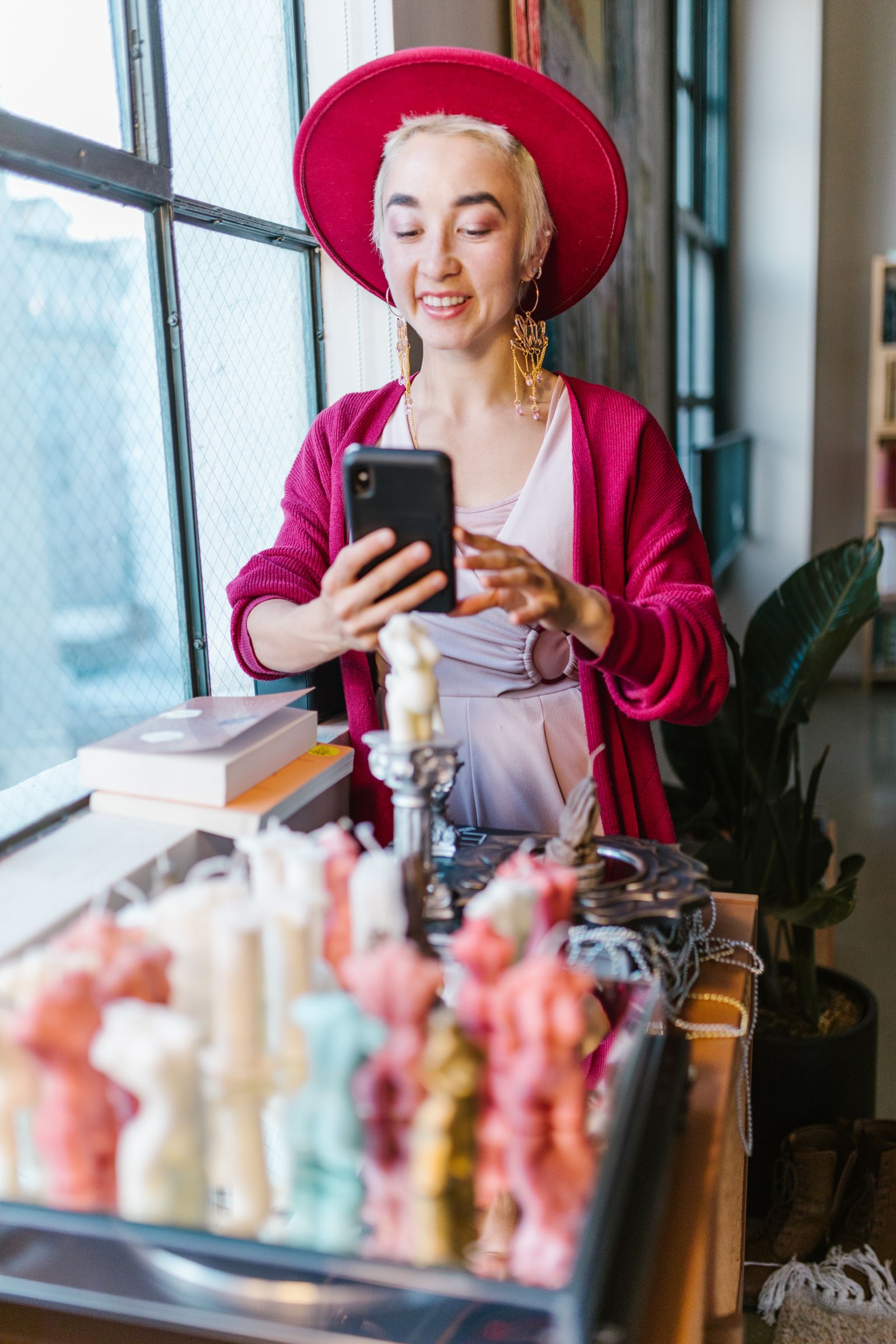 Small business owner photographing handmade candles with a smartphone inside her shop.