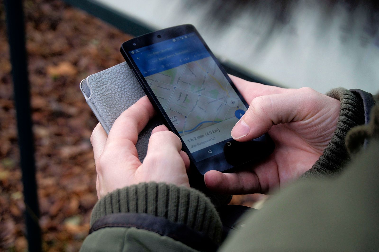 Close-up of hands holding a smartphone displaying a map application outdoors.