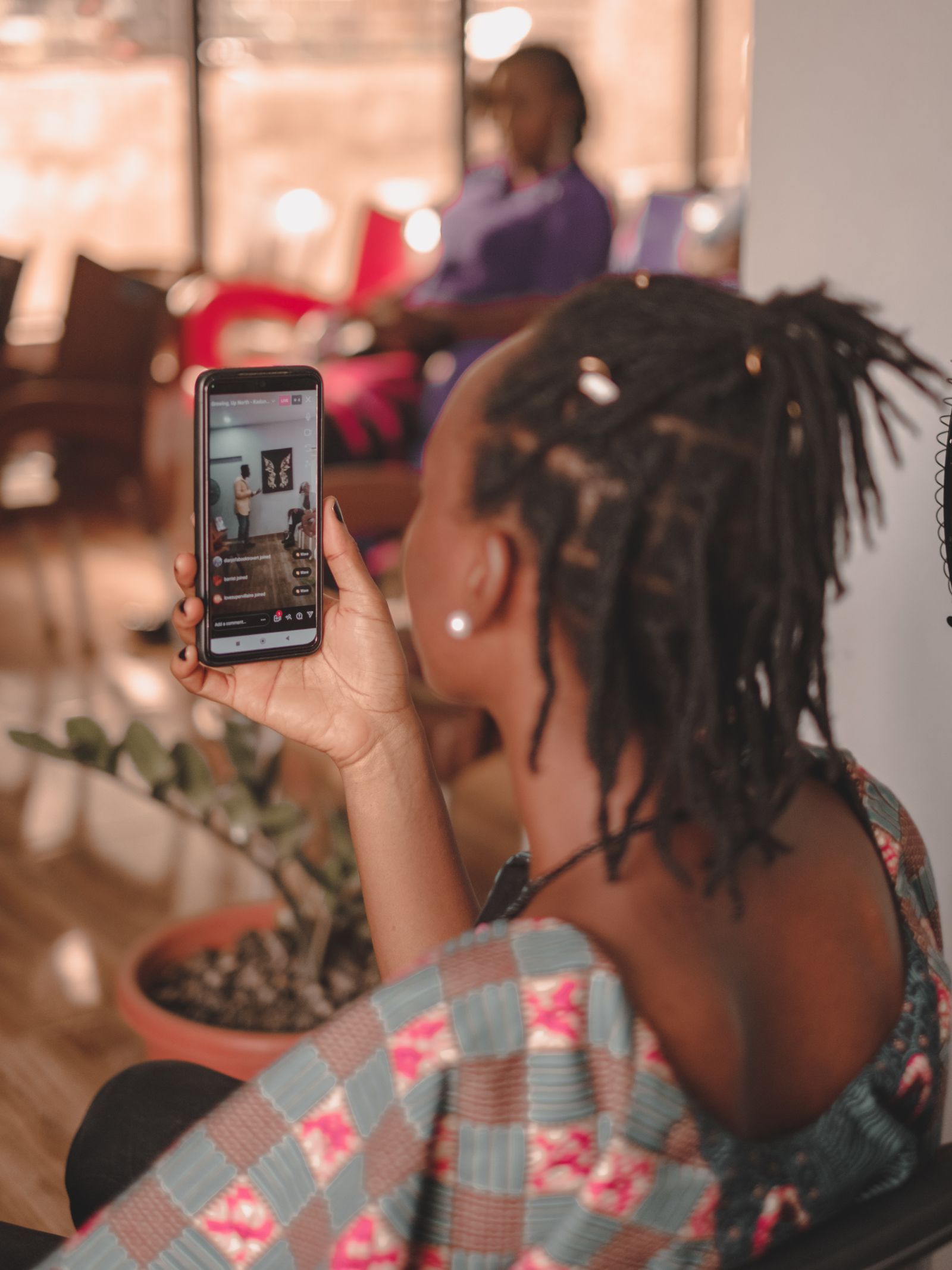 A woman watching a video on her smartphone in a bright, cozy indoor setting.