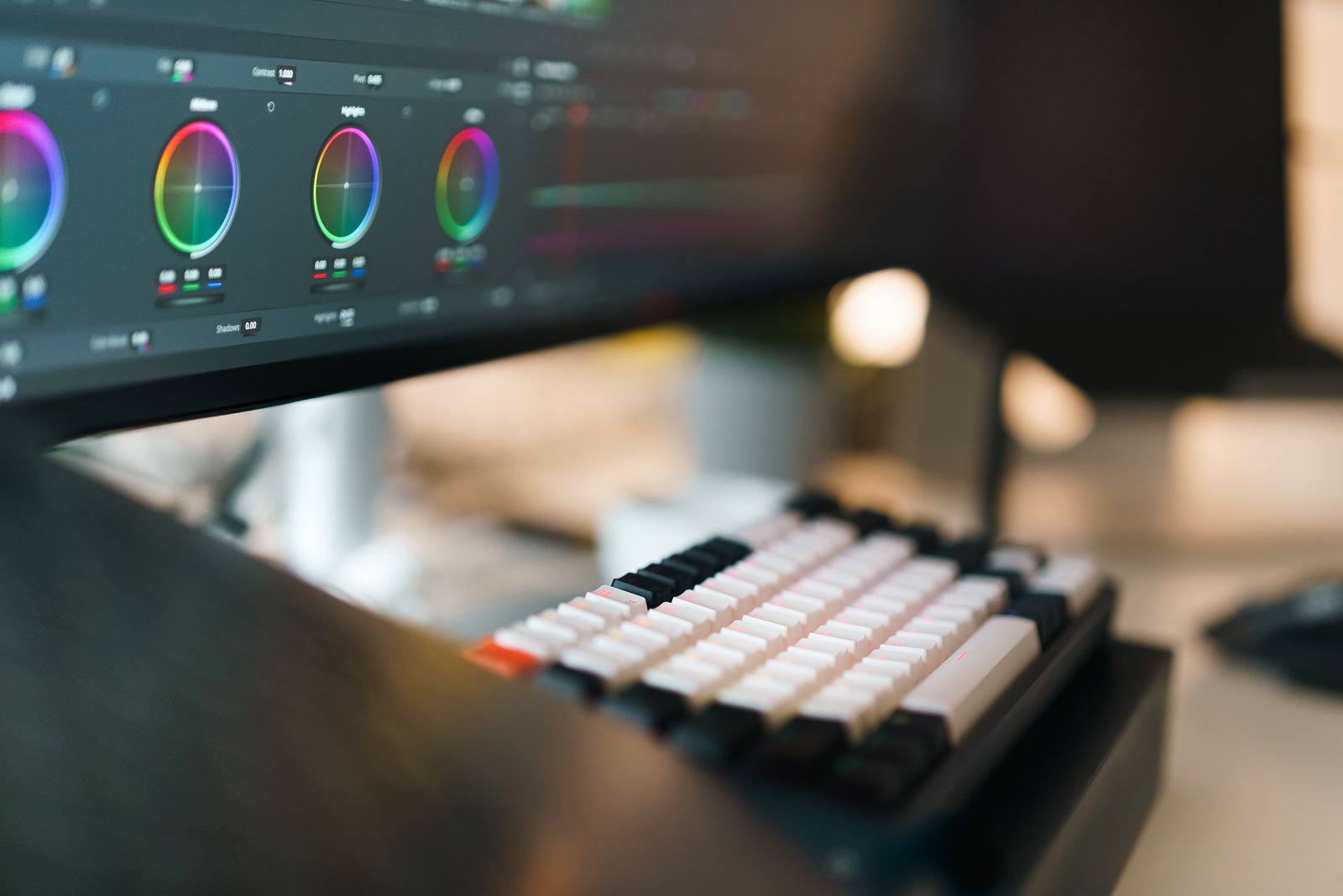 Video editing workstation with a mechanical keyboard and a monitor showing colour grading.