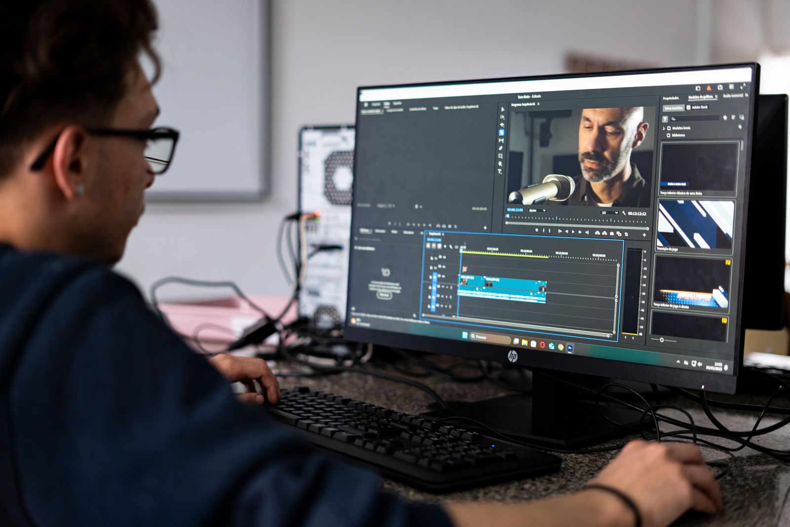 A video editor working at a desktop computer in a modern office, reviewing a project on screen.
