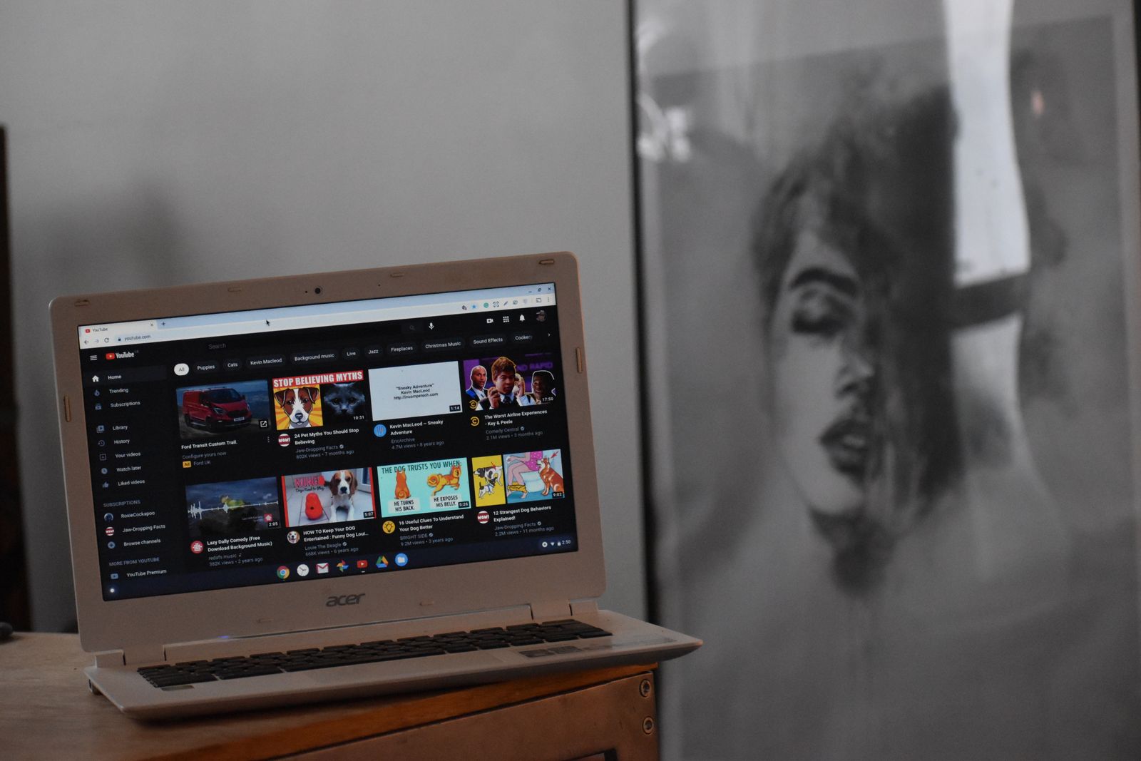 A laptop on a wooden table displaying the YouTube homepage in a warmly lit room.