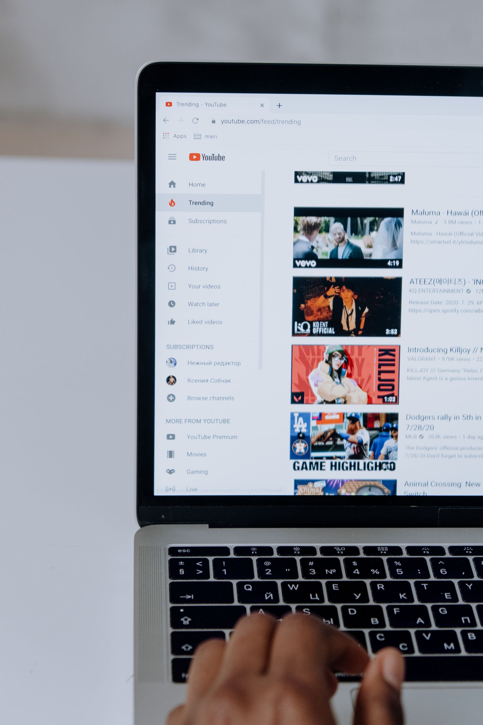 Close-up of a person's hands on a laptop keyboard while browsing YouTube video thumbnails on screen.